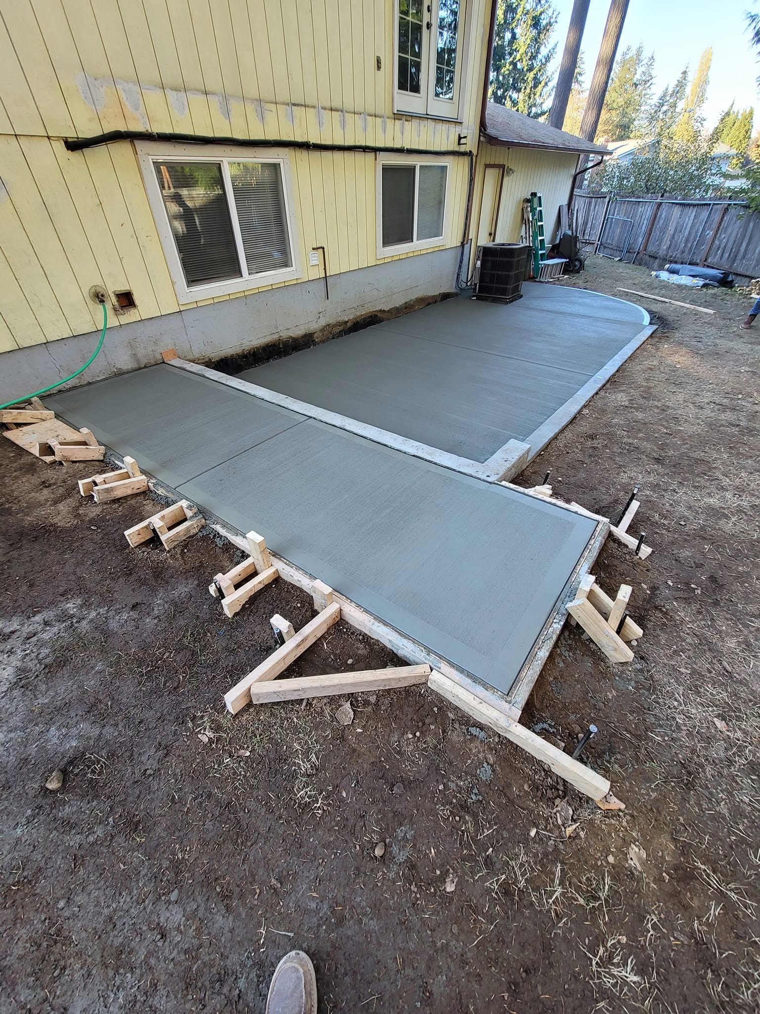 Freshly poured concrete patio slab beside a residential home
