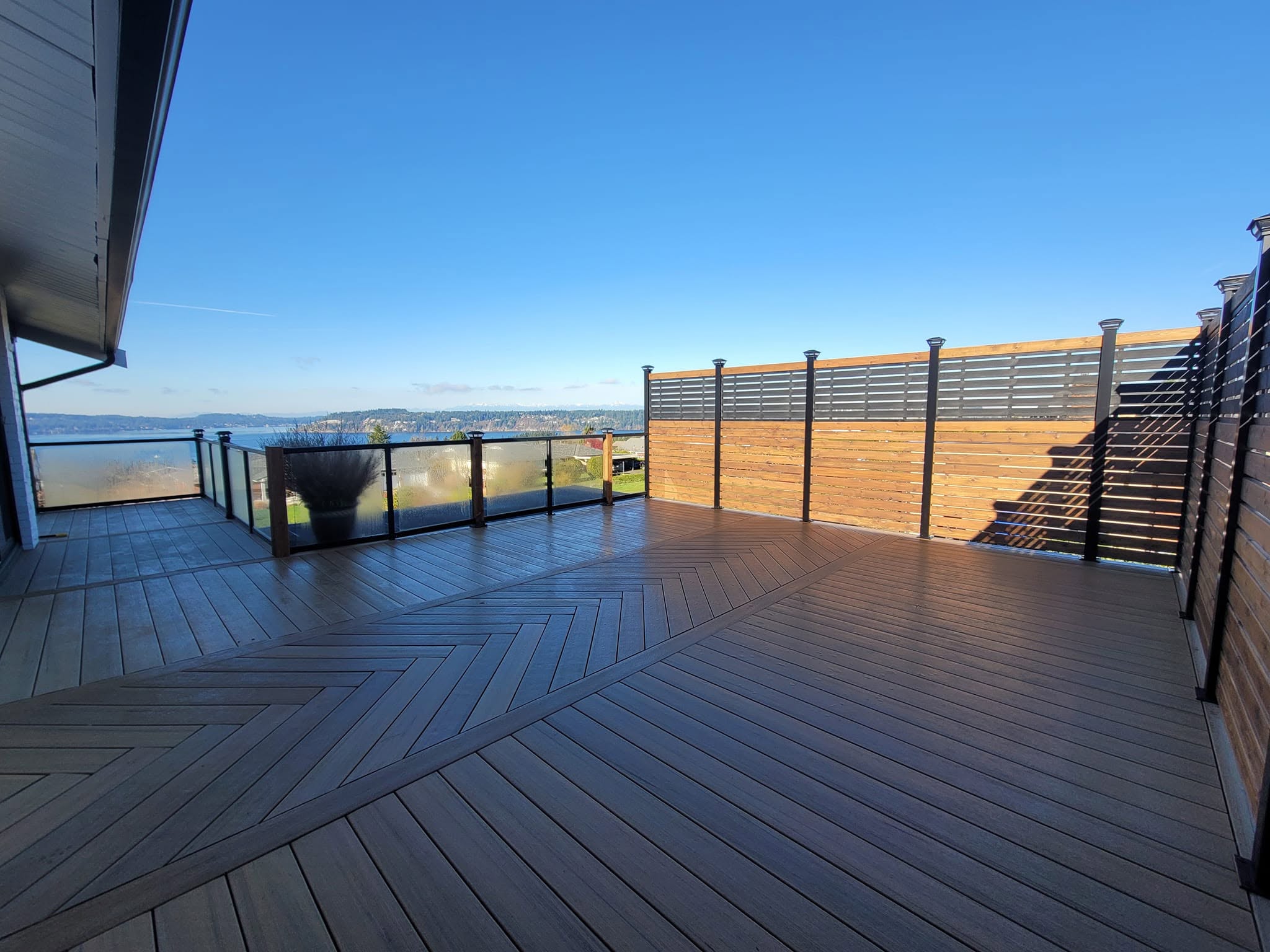 Rooftop composite deck with chevron inlay pattern and glass panel railing overlooking the water