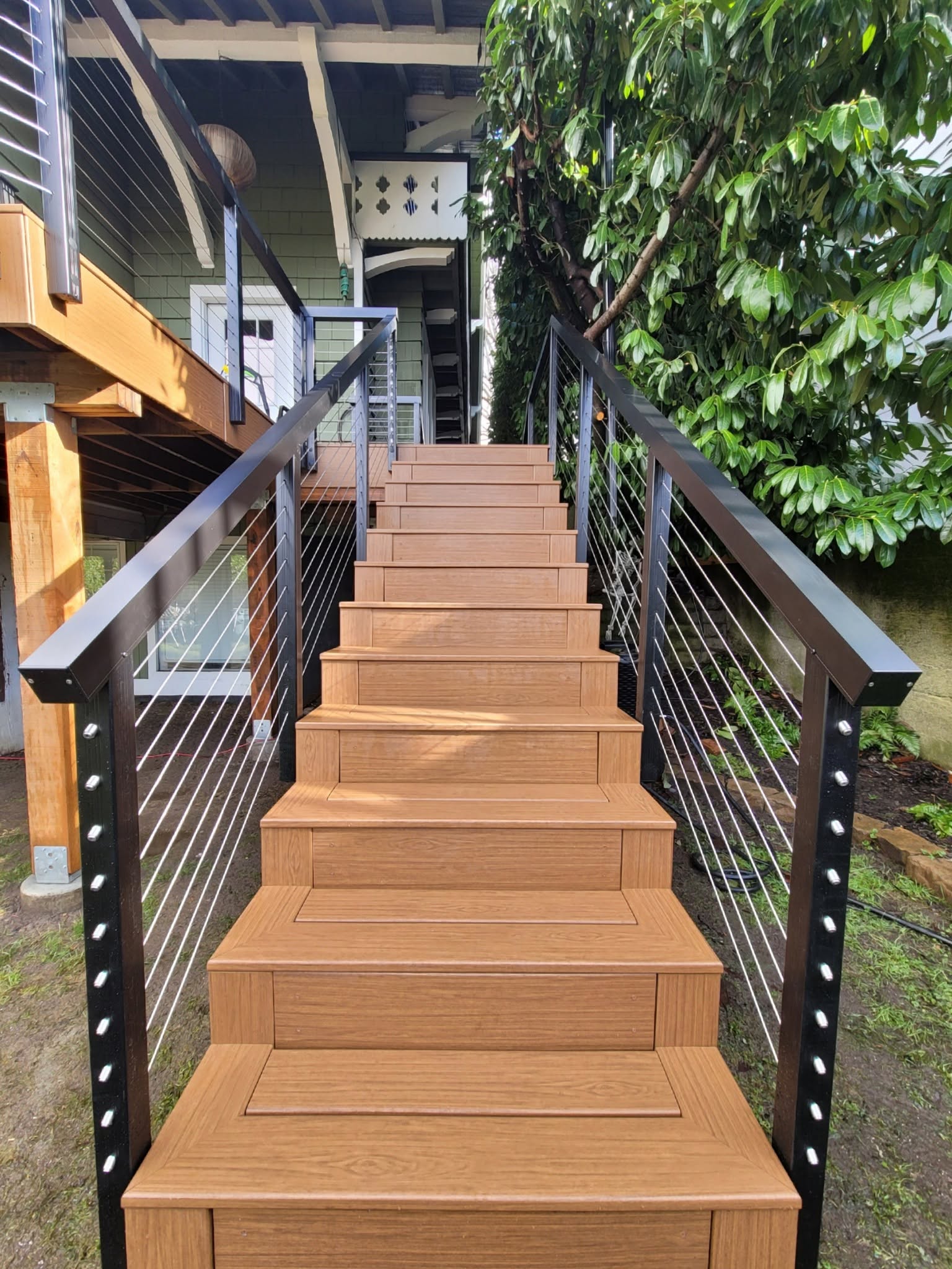 Cable railing staircase with black metal posts connecting upper deck to yard