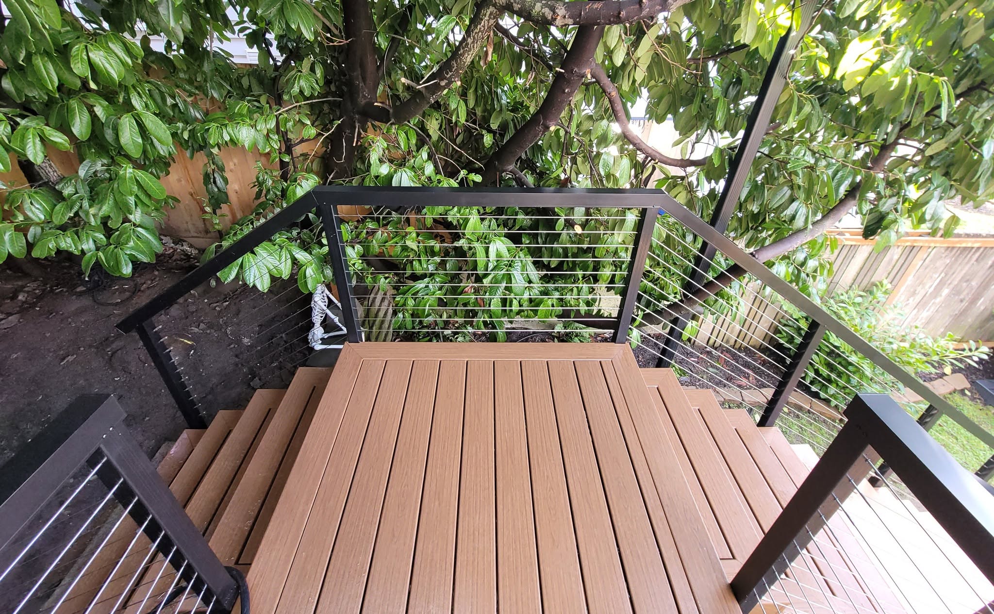 Composite deck with cable railing staircase and lush backyard setting