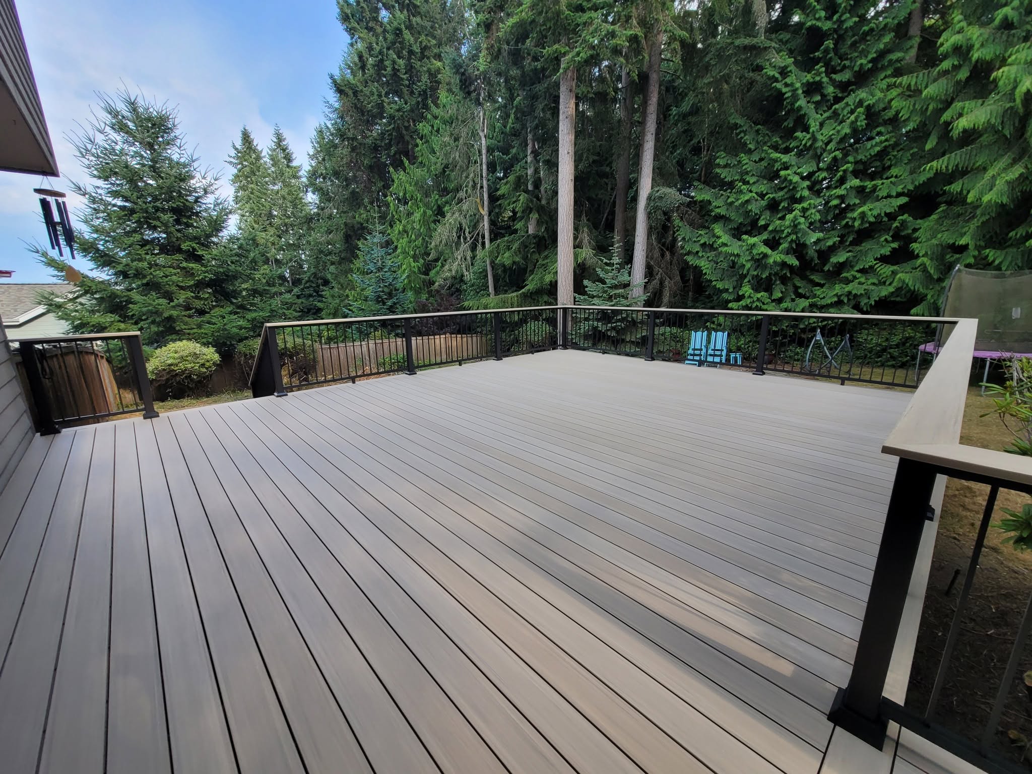 Finished composite deck with black metal railings surrounded by tall evergreens
